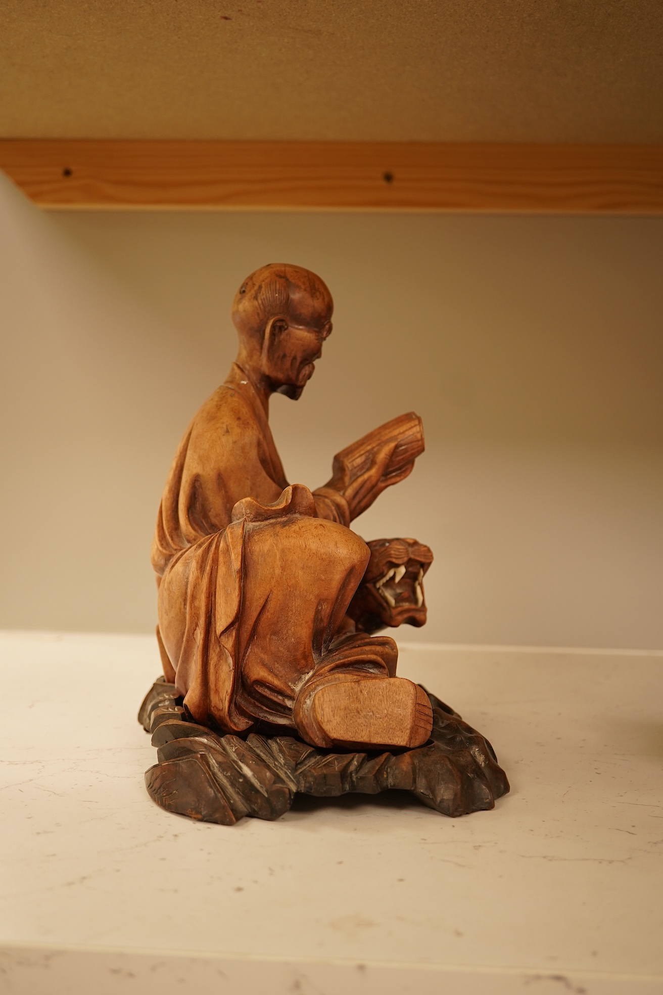 A Chinese hardwood carving of a seated luohan and tiger on hardwood stand, 24cm high including stand.